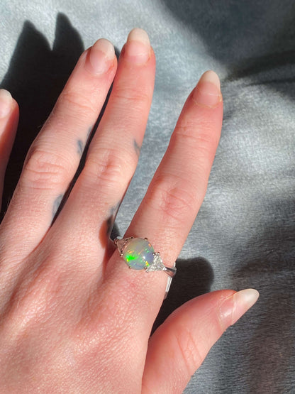 Antique Opal and Trillion Cut Diamond RingDiscover an incredible opal find with this stunning 18k white gold three-stone ring! Featuring a mesmerizing, almost 10mm opal cabochon as its center stone, this ring is a future heirloom in the making. The opal i