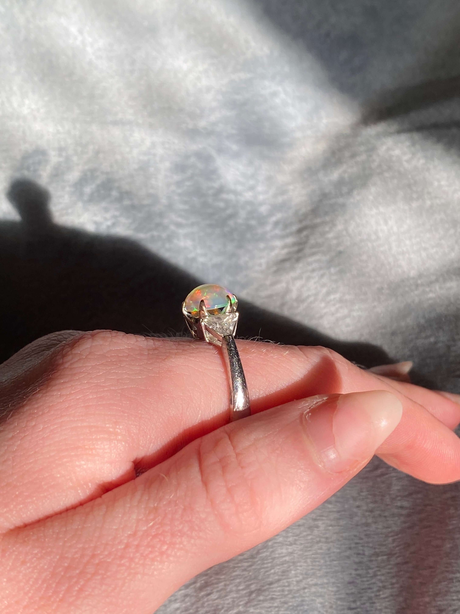 Antique Opal and Trillion Cut Diamond RingDiscover an incredible opal find with this stunning 18k white gold three-stone ring! Featuring a mesmerizing, almost 10mm opal cabochon as its center stone, this ring is a future heirloom in the making. The opal i