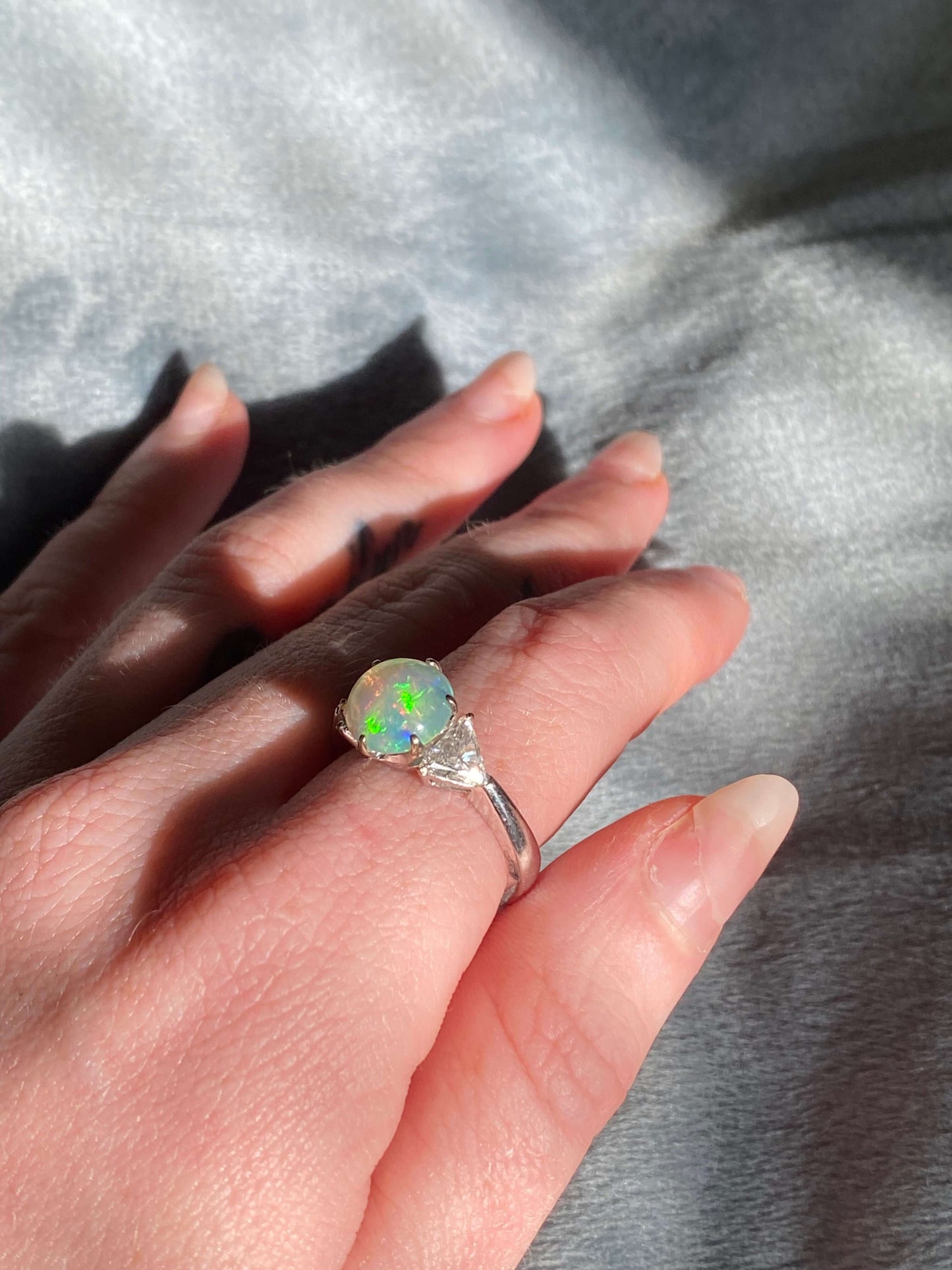 Antique Opal and Trillion Cut Diamond RingDiscover an incredible opal find with this stunning 18k white gold three-stone ring! Featuring a mesmerizing, almost 10mm opal cabochon as its center stone, this ring is a future heirloom in the making. The opal i