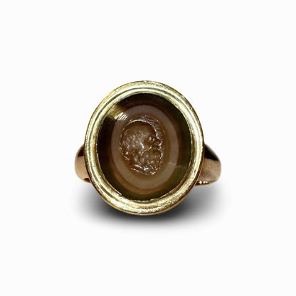 ROMAN INTAGLIO RING BANDED AGATEThe Oval stone engraved with the portrait head of a philosopher, perhaps Socrates, with a bald plate, long hair at the side, a pug nose and a full beard. Mounted as a ring, 19th century gold setting. • Roman Empire; 1st Cen